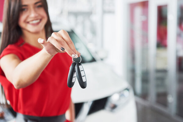 Smiling car salesman handing over your new car keys, dealership and sales concept. Happy girl the buyer